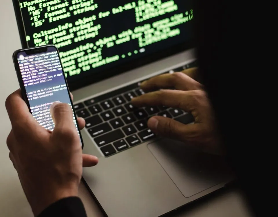 Free Unrecognizable hacker with smartphone typing on laptop at desk Stock Photo
