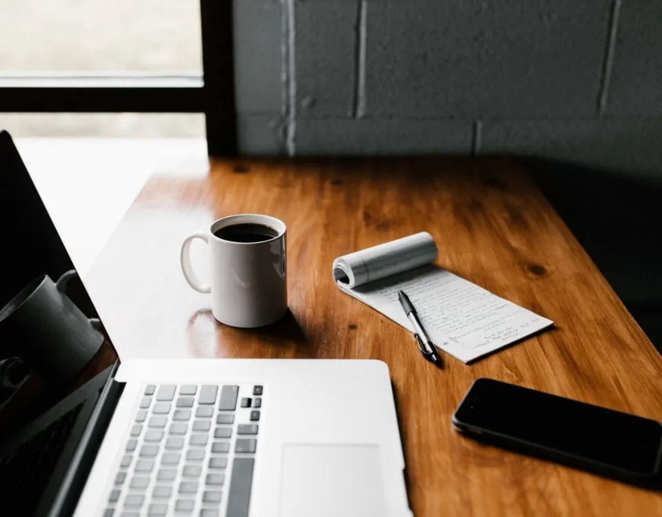 MacBook Pro, white ceramic mug,and black smartphone on table